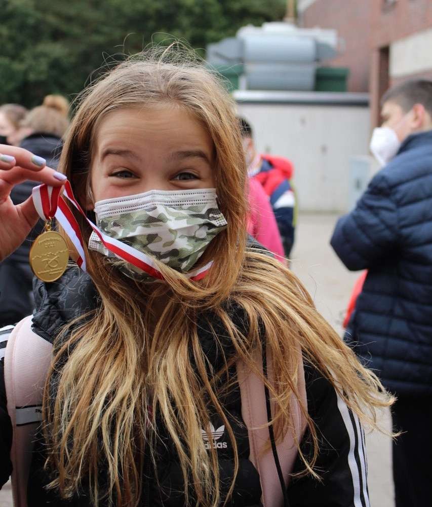 Ein Mädchen mit Maske hält ihre Medaille in die Kamera und freut sich. - Foto: BSN / Udo Schulz