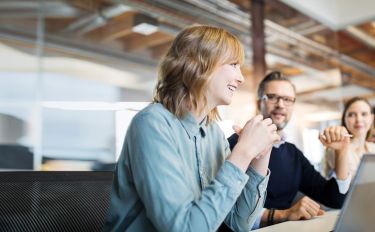 Junge Frau beim Lachen mit Kollegen im Büro.