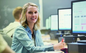 Studentin sitzt am PC und lächelt in die Kamera.