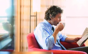 Ein Mann sitzt in einem Sessel, trinkt Kaffee und liest Zeitung.