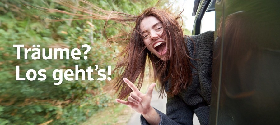 SG_Dreams-2025_HERO_TEXT_900x403 Frau mit braunen Haaren hält ihren Kopf aus dem fahrenden Auto und freut sich.