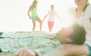 Mann und Frau relaxen am Strand, im Hintergrund spielen die Kinder. - Quelle: DSV, Cultura